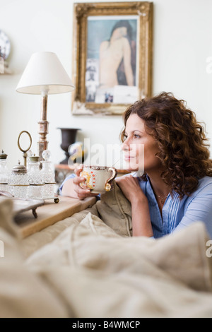 Femme sur un canapé, holding Coffee cup Banque D'Images