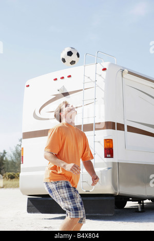 Jeune homme jouant avec un ballon de football sur plage Banque D'Images