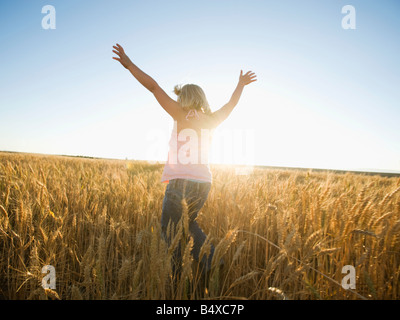 Girl jumping in tall wheat field Banque D'Images