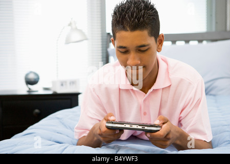 Teenage Boy Lying On Bed Playing Video Game Banque D'Images