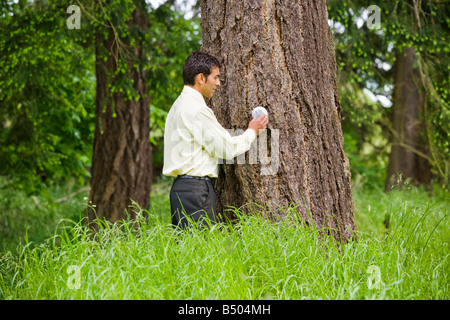Un homme d'origine ethnique mixte de réglage d'un thermostat sur un arbre à l'extérieur Banque D'Images