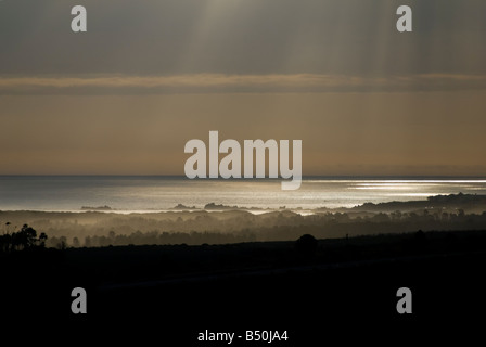 Rayons de soleil céleste brisant les nuages et lumière sur l'eau. Faisceaux de lumière réfléchissant sur l'océan avant le coucher du soleil. Banque D'Images