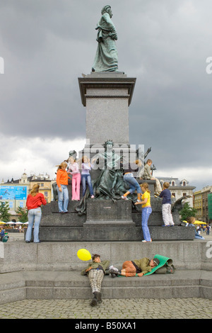 Les enfants de grimper sur le Monument à Adam Mickiewicz la place principale du marché de Cracovie avec un couple de jeunes gens à dormir. Banque D'Images