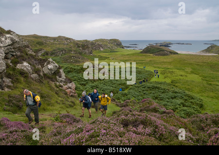 Une longue file de personnes sur le pèlerinage hebdomadaire autour de Iona gravir la colline couverte de bruyère de St Columba's Bay Banque D'Images