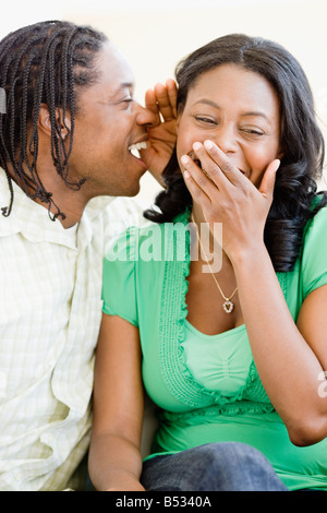 African man whispering in woman's ear Banque D'Images