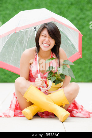 Asian woman sitting sous la pluie parapluie Banque D'Images