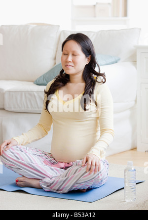 Pregnant Asian woman meditating on yoga mat Banque D'Images