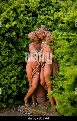 Statue en terre cuite de trois femmes par une haie d'If Banque D'Images