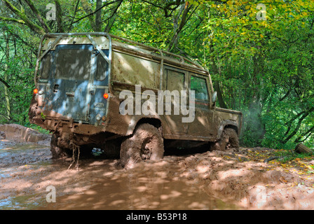 Land Rover Defender 110 boueux en passant par la boue profonde sur une piste forestière dans le Weserbergland. Banque D'Images