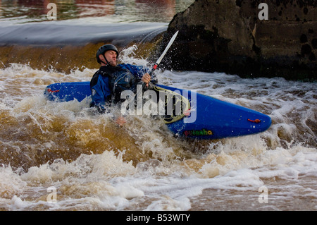 Kayakiste mâle caucasien dans un kayak bleu chavirement dans l'eau blanche. Banque D'Images