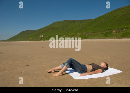 Jeune femme sur une serviette de bain de soleil sur la plage, Rhossili Beach, péninsule de Gower, au Pays de Galles, en Grande-Bretagne, en Europe Banque D'Images