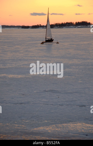 Un iceboat glisse dans le port de Charlottetown sur la rive avec un coucher du soleil doré à l'arrière-plan Banque D'Images