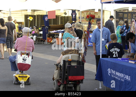 Un couple de personnes âgées bénéficie d'un voyage à un événement public à leur mobilité scooter et fauteuil roulant motorisé. Banque D'Images