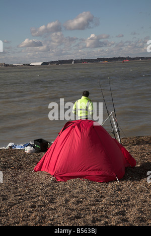 Man with red tente la pêche sur plage sur la rivière Orwell à côté de port de Felixstowe, Suffolk, Angleterre Banque D'Images