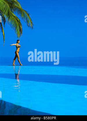 L'équilibrage de femme au bord de la piscine à débordement, Maldives, océan Indien, Asie Banque D'Images