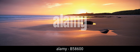 Vue le long de la baie Embleton au lever du soleil, avec silhouette de Château de Dunstanburgh dans la distance, Northumberland, England Banque D'Images