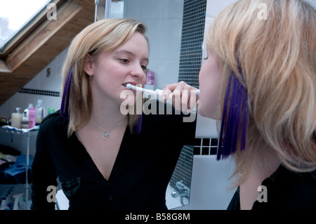 Jeune adolescent ou une femme de ménage se brosser les dents avec une brosse à dents électrique dans sa salle de bains, UK Banque D'Images