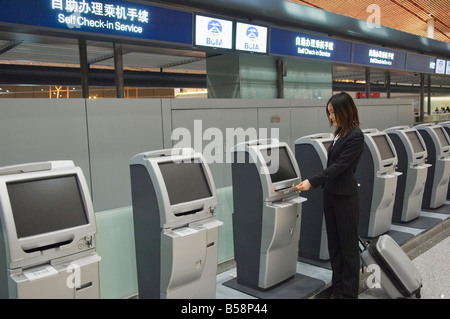 Une femme d'affaires chinois en utilisant le libre service vérifier dans les machines à Beijing Capital Airport, Beijing, Chine Banque D'Images