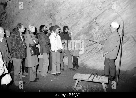 L'industrie minière : : 'Britain's Beauty Spot plus laid' : Blaenau Ffestiniog, un village de mineurs d'ardoise galloise, où les chefs des scories giat tour Ardoise haut au-dessus des toits et plonger jusqu'aux portes des maisons, est devenu une des principales attractions touristiques. Plus de 2 000 touristes par jour troupeau de faire une visite guidée autour de la mine d'Ardoise de Llechwedd - menées par les mineurs, les mêmes hommes qui avaient l'habitude d'une griffe peu dangereux et vivre de la montagne lors de l'extraction de l'ardoise est à son apogée. Un groupe d'au plus profond de la mine l'écoute de leur Guide. Septembre 1975 75-04947-009 Banque D'Images