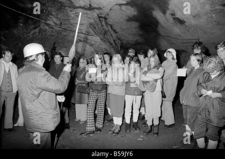 L'industrie minière : : 'Britain's Beauty Spot plus laid' : Blaenau Ffestiniog, un village de mineurs d'ardoise galloise, où les chefs des scories giat tour Ardoise haut au-dessus des toits et plonger jusqu'aux portes des maisons, est devenu une des principales attractions touristiques. Plus de 2 000 touristes par jour troupeau de faire une visite guidée autour de la mine d'Ardoise de Llechwedd - menées par les mineurs, les mêmes hommes qui avaient l'habitude d'une griffe peu dangereux et vivre de la montagne lors de l'extraction de l'ardoise est à son apogée. Un groupe d'au plus profond de la mine l'écoute de leur Guide. Septembre 1975 75-04947-011 Banque D'Images