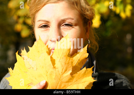 Jolie jeune femme se cache derrière les feuilles d'or Banque D'Images