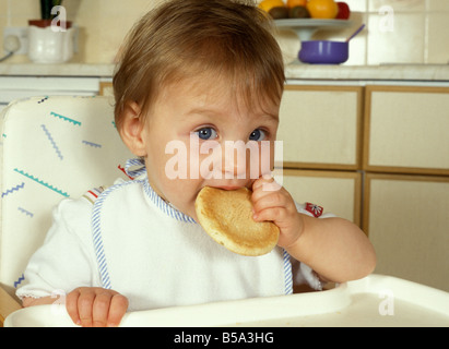 Jeune bébé dans une chaise haute manger rusk Banque D'Images