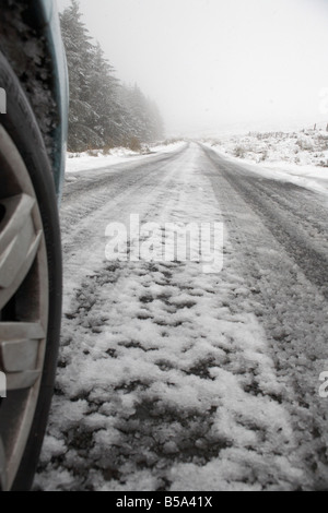 Roue de voiture et de la neige et de la glace sur une route de montagne rurales éloignées passé en courant une forêt dans le comté d'Antrim en Irlande du Nord uk Banque D'Images