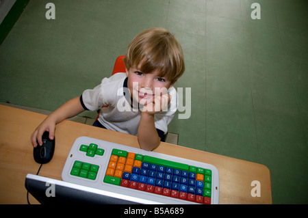 Smiling infant garçon lève les yeux de son ordinateur à l'école maternelle spécial Banque D'Images