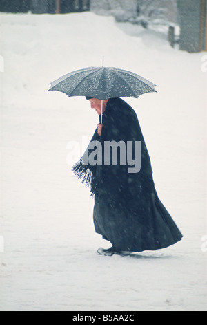 Vieille Femme avec châle et parapluie marcher dans la neige en hiver Banque D'Images