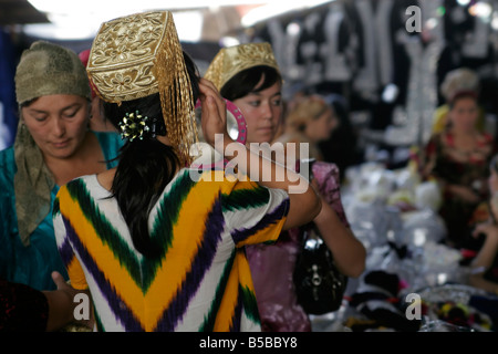 Jeune femme ouzbek essayant sur mariage traditionnel skullcap, marché du dimanche de Urgut, l'Ouzbékistan, en Asie centrale Banque D'Images