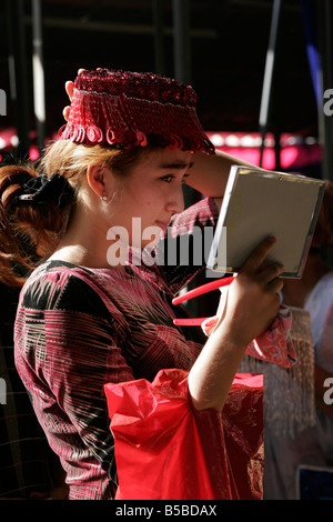 Jeune femme ouzbek essayant sur mariage traditionnel skullcap, marché du dimanche de Urgut, l'Ouzbékistan, en Asie centrale Banque D'Images