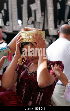 Jeune femme ouzbek essayant sur mariage traditionnel skullcap, marché du dimanche de Urgut, l'Ouzbékistan, en Asie centrale Banque D'Images