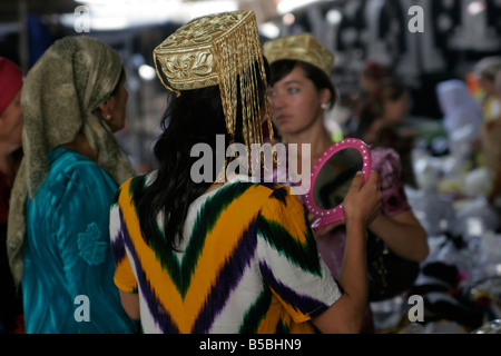 Jeune femme ouzbek essayant sur mariage traditionnel skullcap, marché du dimanche de Urgut, l'Ouzbékistan, en Asie centrale Banque D'Images