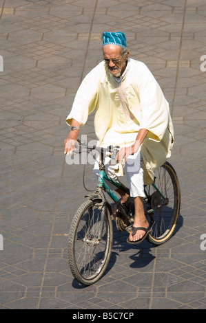 Un homme âgé portant un costume traditionnel équitation sa bicyclette à la place Djemaa El Fna - la place du marché de Marrakech. Banque D'Images