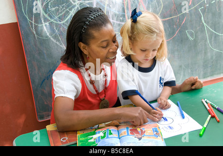 L'encadrement de l'enseignant la fille à attirer et reconnaît les formes à l'extérieur de la région de sunny ecole maternelle playschool Banque D'Images