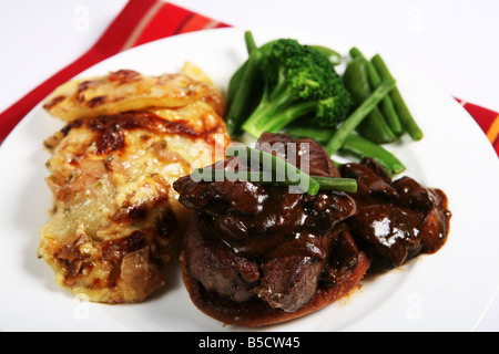 Un repas de boeuf tournedos sur un croûton garni de champignons dans une sauce brune avec des haricots,petits pois et l'oignon et de pommes de terre au gratin Banque D'Images