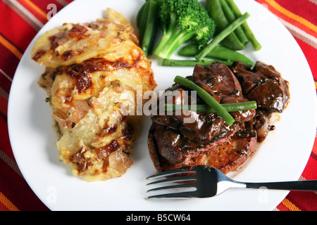 Un repas de boeuf tournedos sur un croûton garni de champignons dans une sauce brune avec des haricots,petits pois et l'oignon et de pommes de terre au gratin Banque D'Images