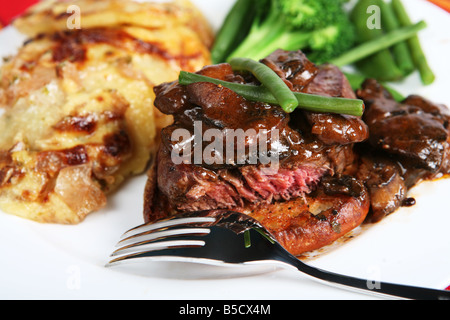 Un repas de boeuf tournedos sur un croûton garni de champignons dans une sauce brune avec des haricots,petits pois et l'oignon et de pommes de terre au gratin Banque D'Images