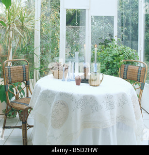 Des chaises en rotin à table circulaire avec un tissu blanc dans la petite véranda salle à manger avec vue sur le jardin via Windows Banque D'Images