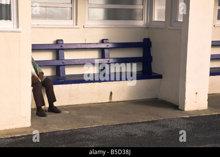 Compte tenu de l'ombre femme âgée assise sur un banc à l'abri du front de mer sur la côte du Dorset. Banque D'Images