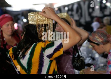 Jeune femme ouzbek essayant sur mariage traditionnel skullcap, marché du dimanche de Urgut, l'Ouzbékistan, en Asie centrale Banque D'Images