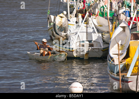 BELIZE CITY BELIZE Man pagaies canoe près de bateaux de pêche amarrés dans le port de Belize à l'embouchure du Haulover Creek Banque D'Images