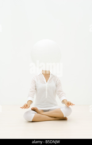 Femme assise en position du lotus, lanterne de papier face obscurcissant Banque D'Images