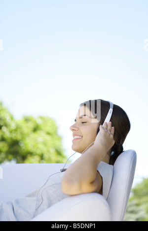 Teenage girl listening to headphones, confortablement assis dans un fauteuil, les yeux fermés Banque D'Images