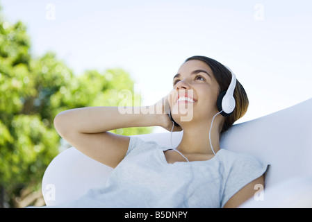 Teenage girl listening to headphones, looking up, smiling Banque D'Images