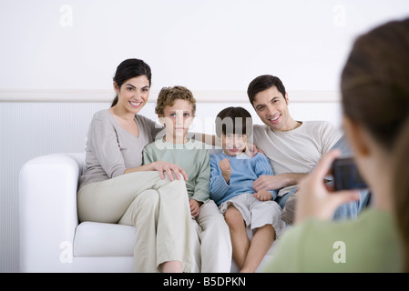 Family sitting on sofa, posant pour la photo prise par sa fille Banque D'Images