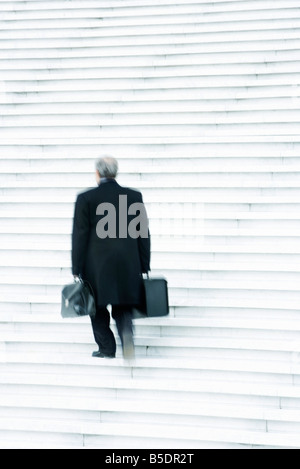 Businessman carrying deux lourds sacs lentement vers le haut des escaliers à l'extérieur Banque D'Images