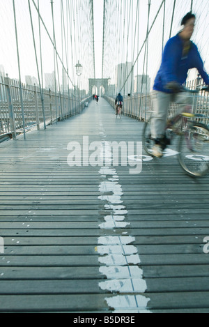 Man riding bike à travers passerelle piétonne du pont de Brooklyn, dans la ville de New York, Manhattan skyline à distance Banque D'Images