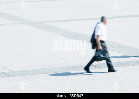 Businessman à la veste sur l'épaule de marcher à travers la place publique Banque D'Images