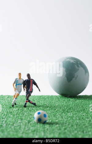 Joueurs de football miniature à la poursuite d'un ballon de football, globe en arrière-plan Banque D'Images